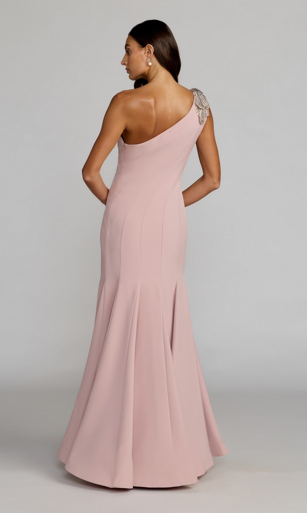 A woman stands with her back to the camera in a floor-length blush pink Beaded-One-Shoulder Prom Gown, Mac Duggal 11810, featuring beaded detail on the shoulder.